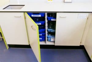 Trespa Benching with yellow contrast edging on cupboard and light and dark blue Gratnells’ Trays inside, holding science beakers.