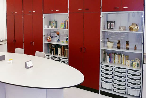Teaching wall space with display cabinet with grey trays and red storage cupboards.